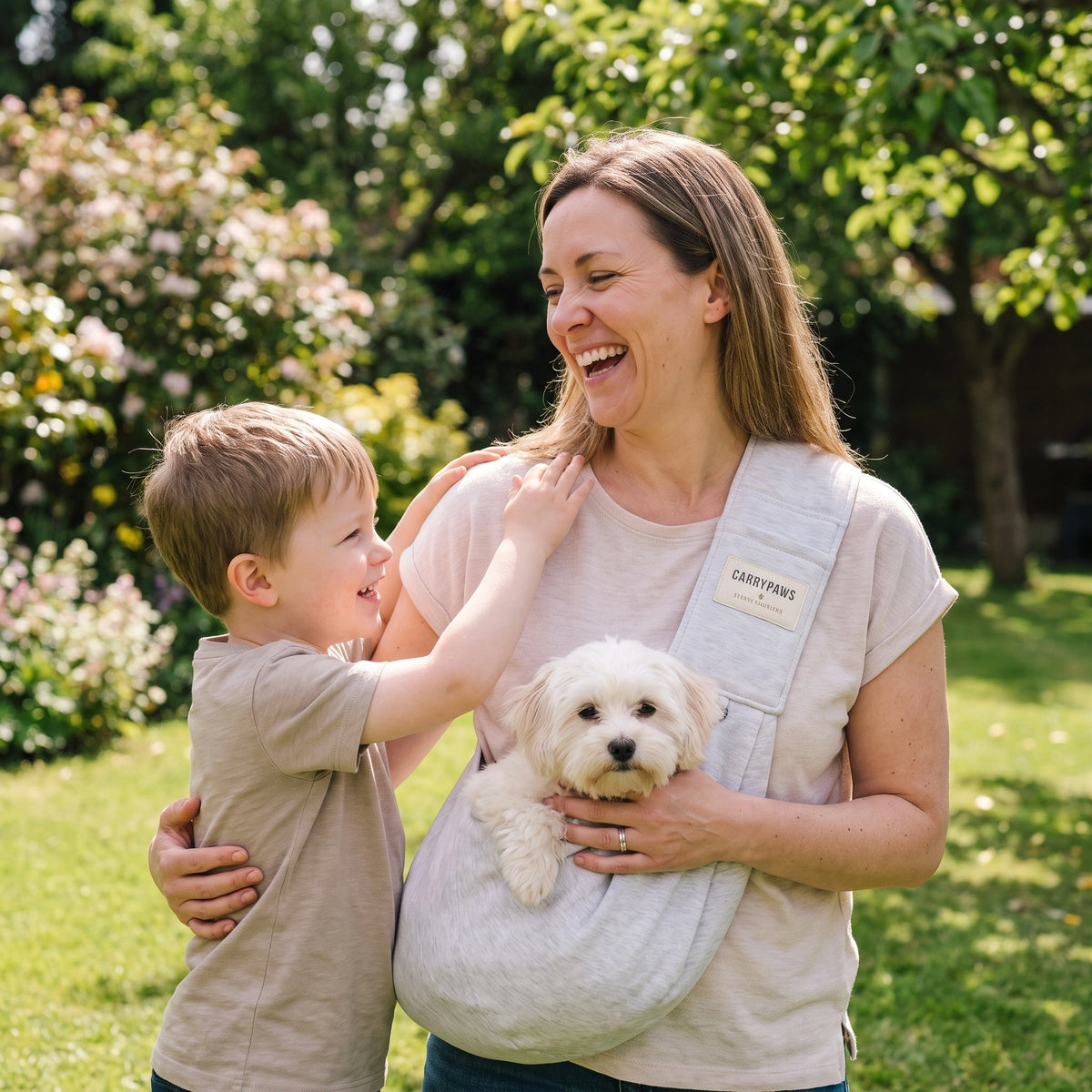 Mother and young son laughing with their small white dog in a light grey CarryPaws dog sling carrier